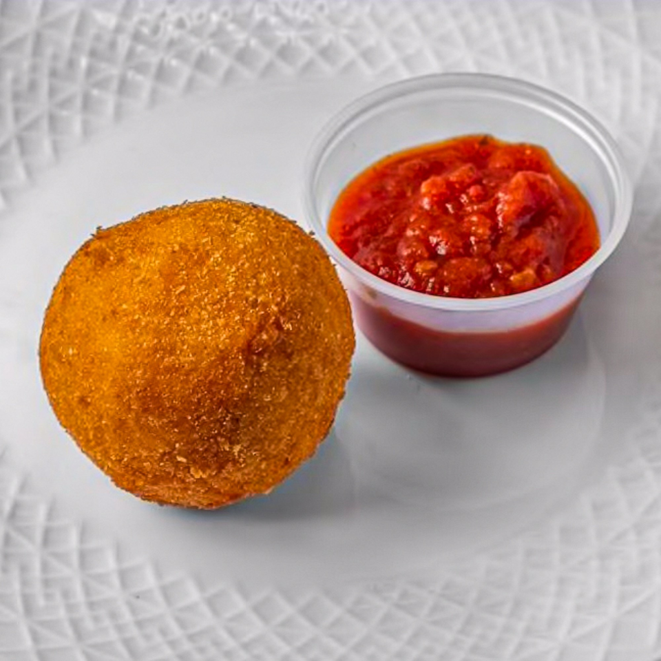 Golden-brown arancini, a fried rice ball, served with a side of red marinara sauce on a white plate.
