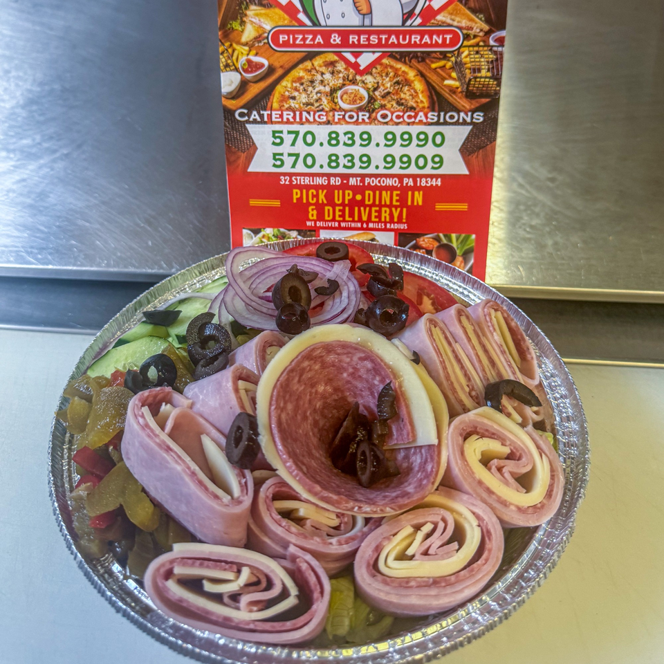 Antipasto salad with rolled meats and cheeses, olives, and vegetables in a foil tray.